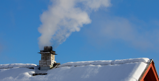 A chimney puffing white smoke from a frost capped roof.